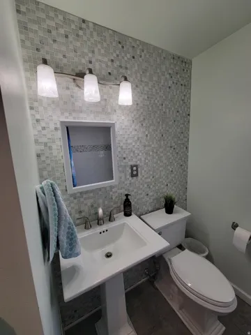Pedestal sink with a brushed nickel faucet, complete with a mosaic tile accent wall and a three-light vanity fixture