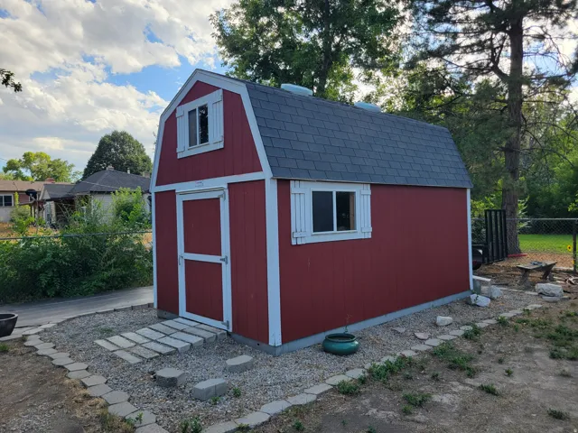 Red shed with a gambrel roof, white trim, and two windows with shutters