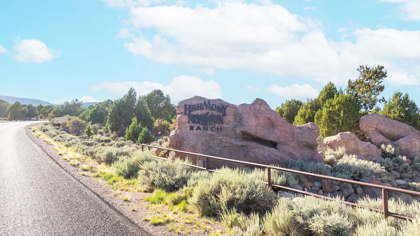 Rock formation signage with "Harmony Mountain Ranch" inscription, framed by varied native vegetation and a paved roadway