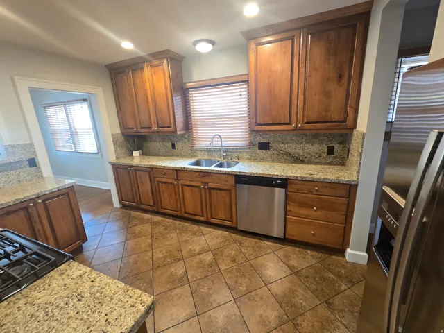 Kitchen featuring granite countertops, wood cabinetry, stainless steel dishwasher, dual basin sink, and tile flooring