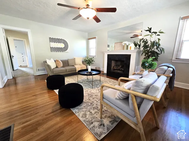 Living area featuring wood-finish flooring, a fireplace with a dark stone surround and white mantel, a large wall-mounted mirror, and a ceiling fan with integrated light fixture