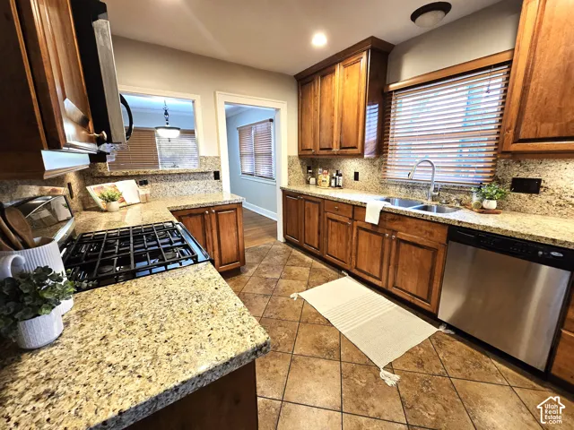 Kitchen featuring custom wood cabinetry, natural stone countertops, a dual-basin stainless steel sink, a gas range, and diamond-pattern tile flooring