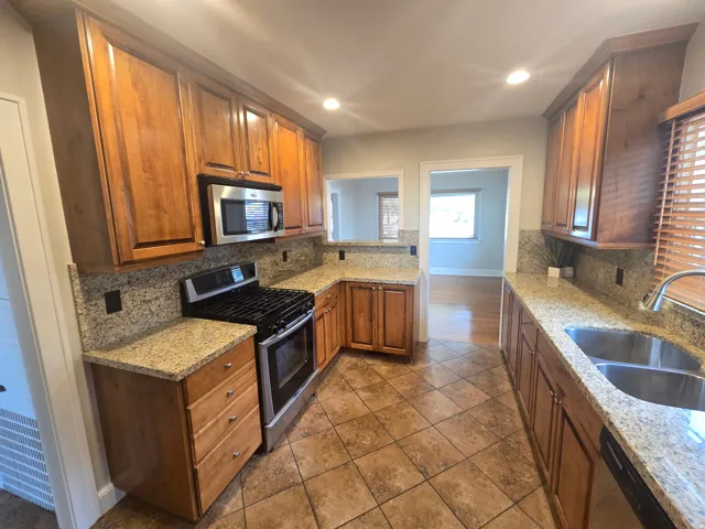 Kitchen featuring wood cabinetry, stainless steel appliances, a double basin sink, stone countertops, and tile flooring