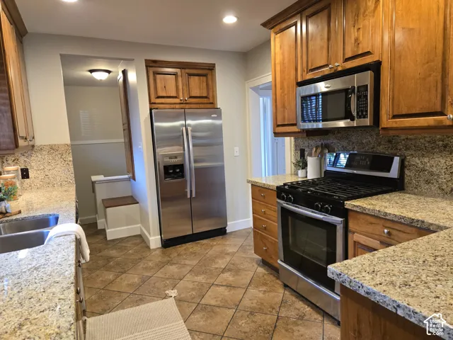 Kitchen featuring medium-tone wood cabinetry, stone countertops, stainless steel appliances, and ceramic tile flooring