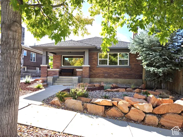 Brick exterior featuring a covered front porch, concrete walkway, and tiered rock landscaping