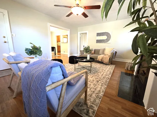 Living area featuring wood-finish flooring, a fireplace with a black tile hearth, and a ceiling fan with integrated lighting