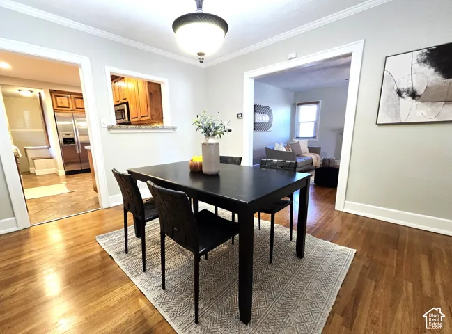 Dining area featuring hardwood flooring, crown molding, a semi-flush mount pendant light, and a pass-through opening to the kitchen