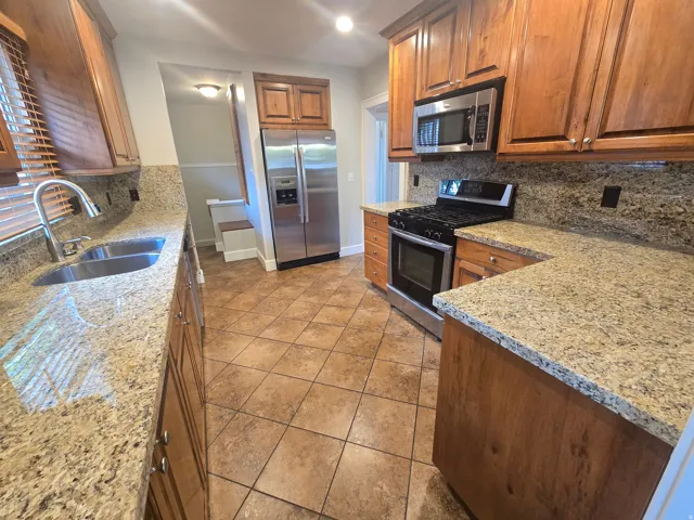 Kitchen featuring wood cabinetry, light-toned countertops, a stainless steel double basin sink, and stainless steel appliances