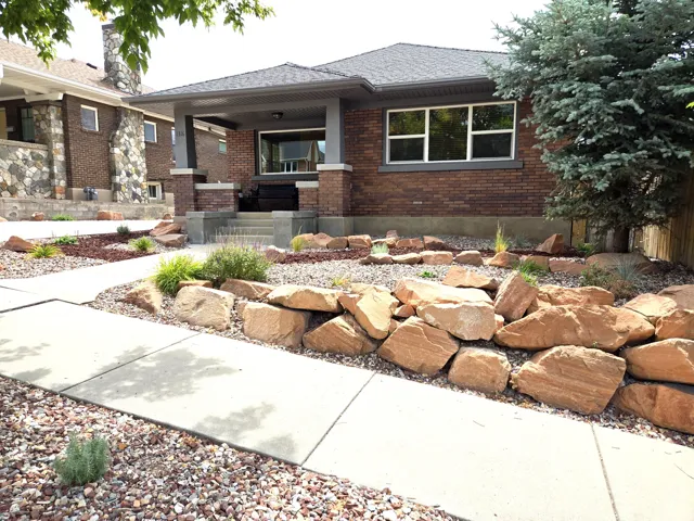 Brick exterior with a covered porch, white-trimmed windows, and a landscaped front yard featuring a rock retaining wall and concrete pathways