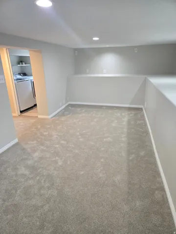 Recessed lighting illuminates the carpeted flooring and light gray walls