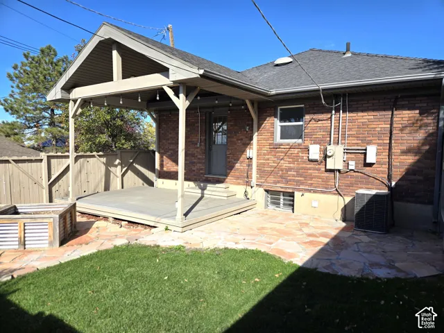 Brick exterior featuring a covered wood deck, flagstone patio, manicured lawn, and wood privacy fencing