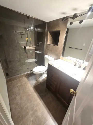 Glass-enclosed shower with a recessed shelf, full-height wall tiling, and a built-in vanity with a stone countertop