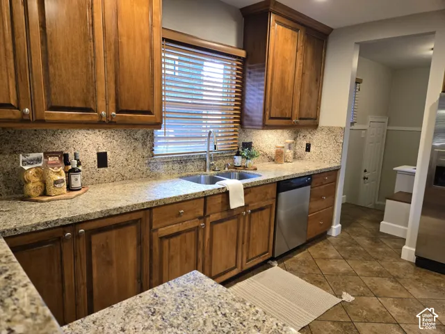 Kitchen featuring stained wood cabinetry, stone-finish countertops, tile flooring, stainless steel dishwasher, and a dual-basin stainless steel sink