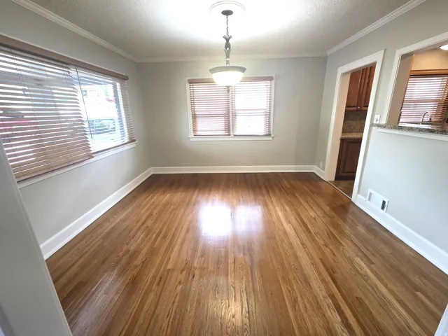 Hardwood flooring extends throughout this room, featuring multiple windows, crown molding, and a chandelier-style light fixture