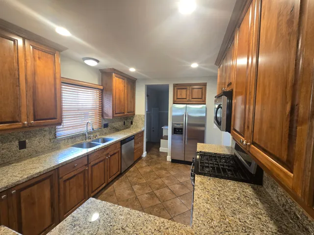 Kitchen featuring wood cabinetry, granite countertops, stainless steel appliances, and tile flooring