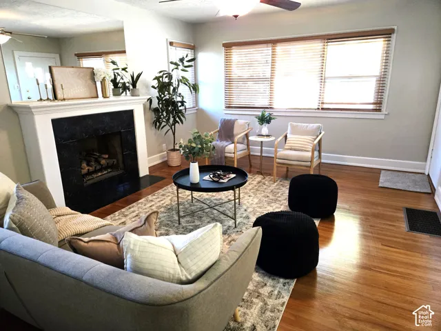 Fireplace featuring a decorative black tile surround and white mantel, large windows with horizontal blinds, and wood-finish flooring