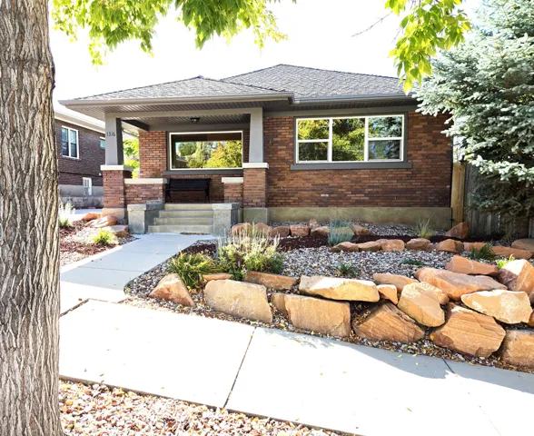 Brick exterior featuring a covered front porch, concrete steps, and landscaped stone retaining walls