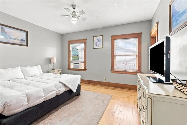 Light gray walls complement the wood-finish flooring, featuring two windows with wood trim