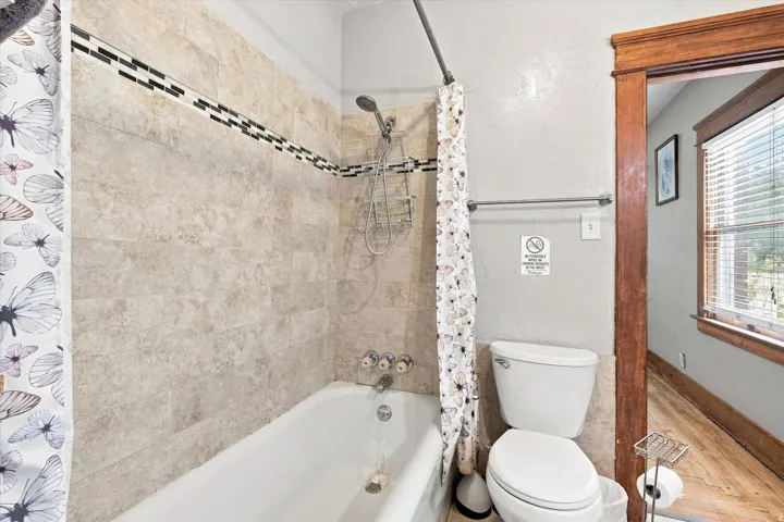 Bathtub with tiled surround, handheld shower fixture, and decorative tile accent