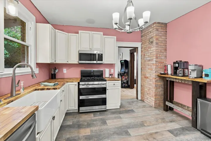 Kitchen featuring wood-finish flooring, white cabinetry, a farmhouse sink, and a brick column