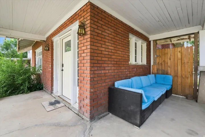 Brick exterior with a covered concrete porch, white entry door with glass pane, and decorative wall-mounted lighting fixtures