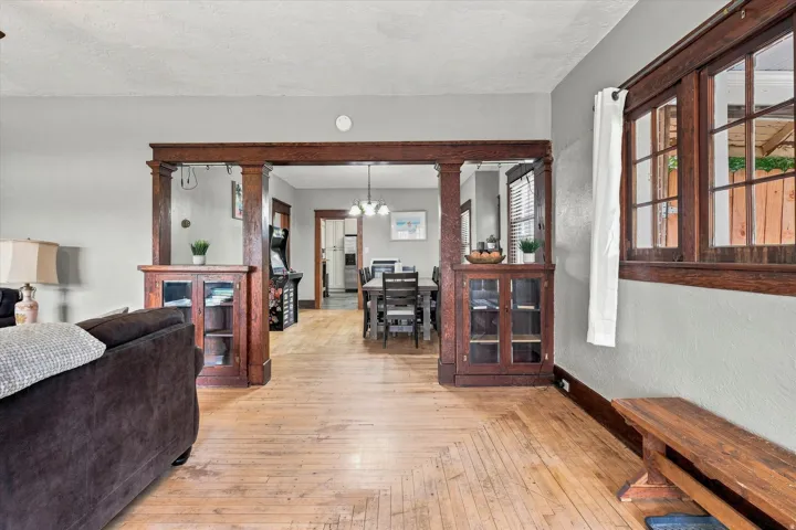Spacious open-concept living area featuring rich wood-finish flooring, decorative wood-beam archways, and substantial built-in cabinetry with glass-front doors