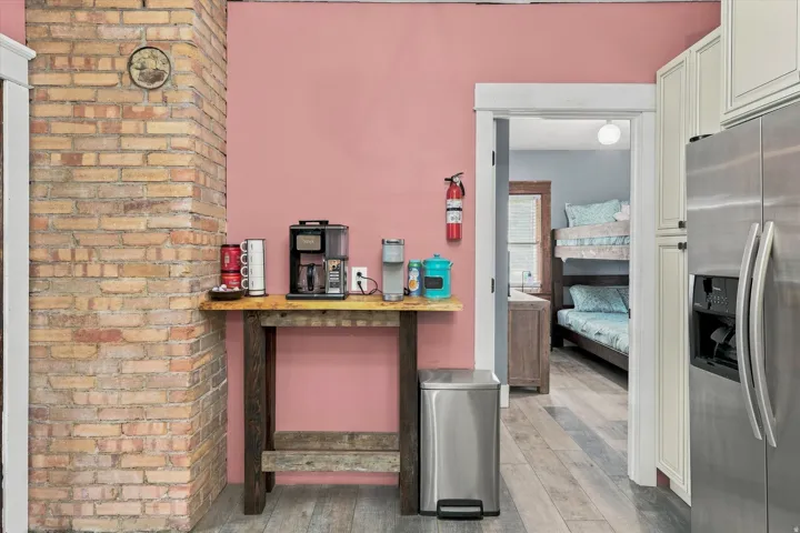 Exposed brick column, wood-finish flooring, stainless steel refrigerator, white cabinetry, and a built-in wood-finish counter
