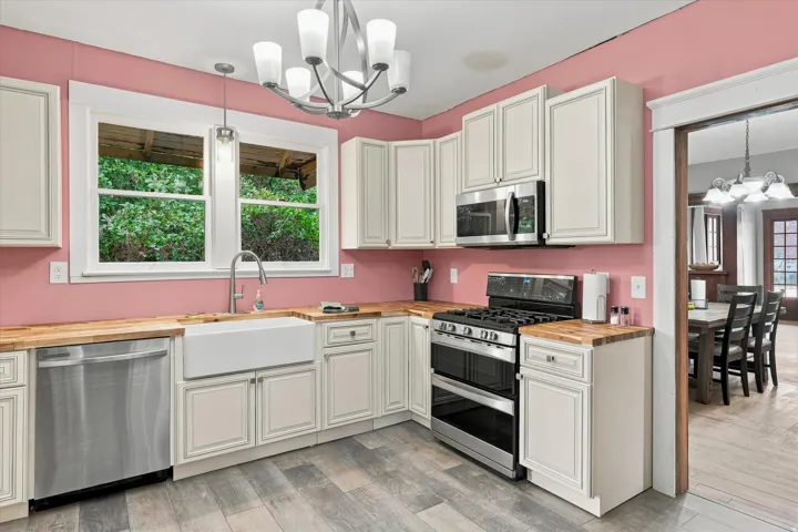 Kitchen featuring light-toned cabinetry, wood-finish countertops, stainless steel appliances, and a farmhouse sink