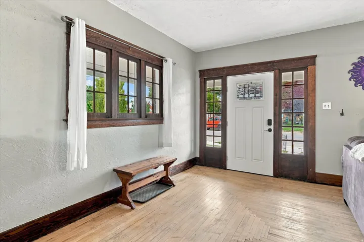 Hardwood flooring, wood-framed window, wood-framed entry door with sidelights, decorative glass insert, and textured walls
