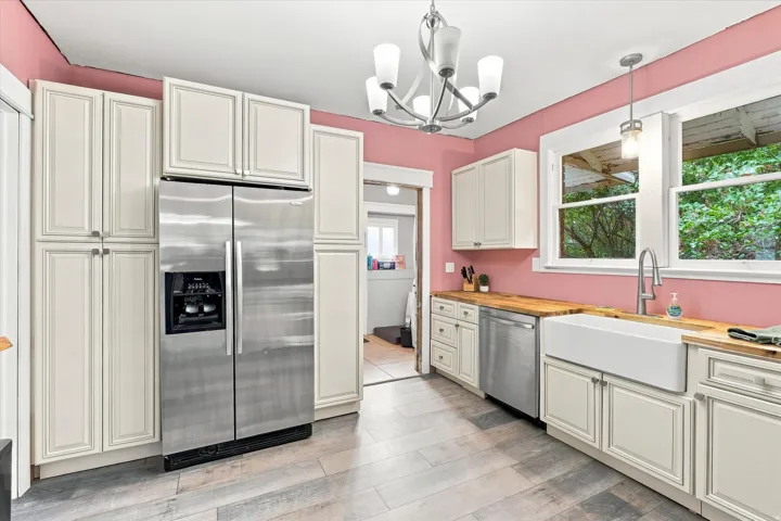 Stainless steel side-by-side refrigerator, white shaker-style cabinetry, wood-finish countertops, ceramic farmhouse sink, and wood-finish flooring