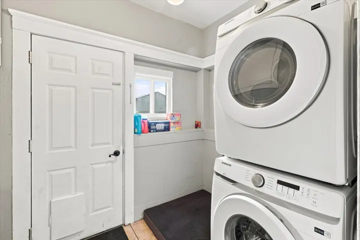 Stackable laundry appliances, multi-pane window, white paneled door, black door hardware, light-colored walls