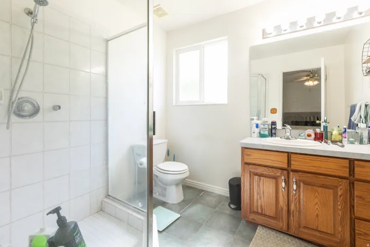 Tiled shower enclosure with a glass door, single vanity with wood-finish cabinetry, and a framed mirror with overhead lighting