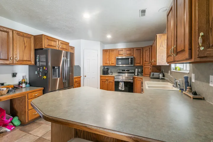 Kitchen featuring wood cabinetry, stainless steel appliances, a composite countertop island, and tile flooring