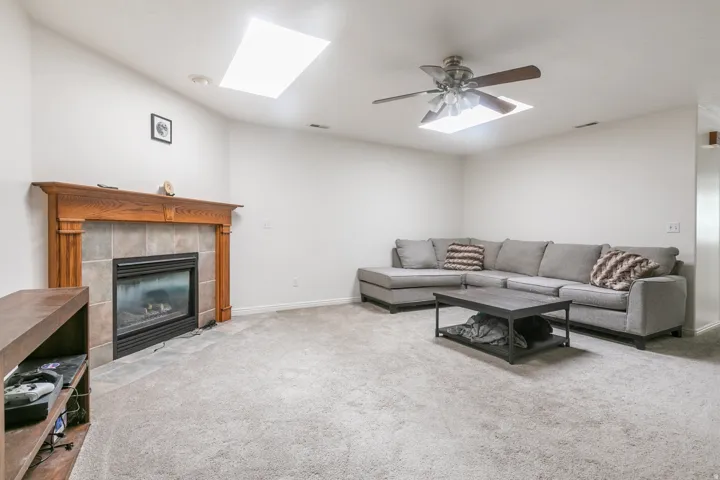 Fireplace with wood mantel and tile surround, two skylights, and ceiling fan with integrated lighting