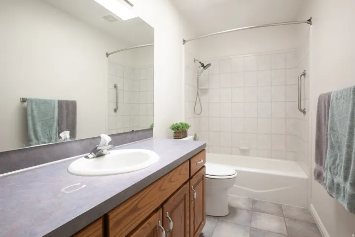 Vanity with integrated sink, wood-finish cabinetry, full-width mirror, tile flooring, and a tiled shower/tub combination