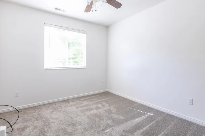 Neutral wall colors, textured carpeting, window with blinds, and ceiling fan with integrated lighting