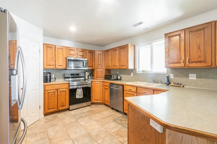 Kitchen featuring wood cabinetry, stainless steel appliances, a double basin sink, ample countertop space, and tile flooring