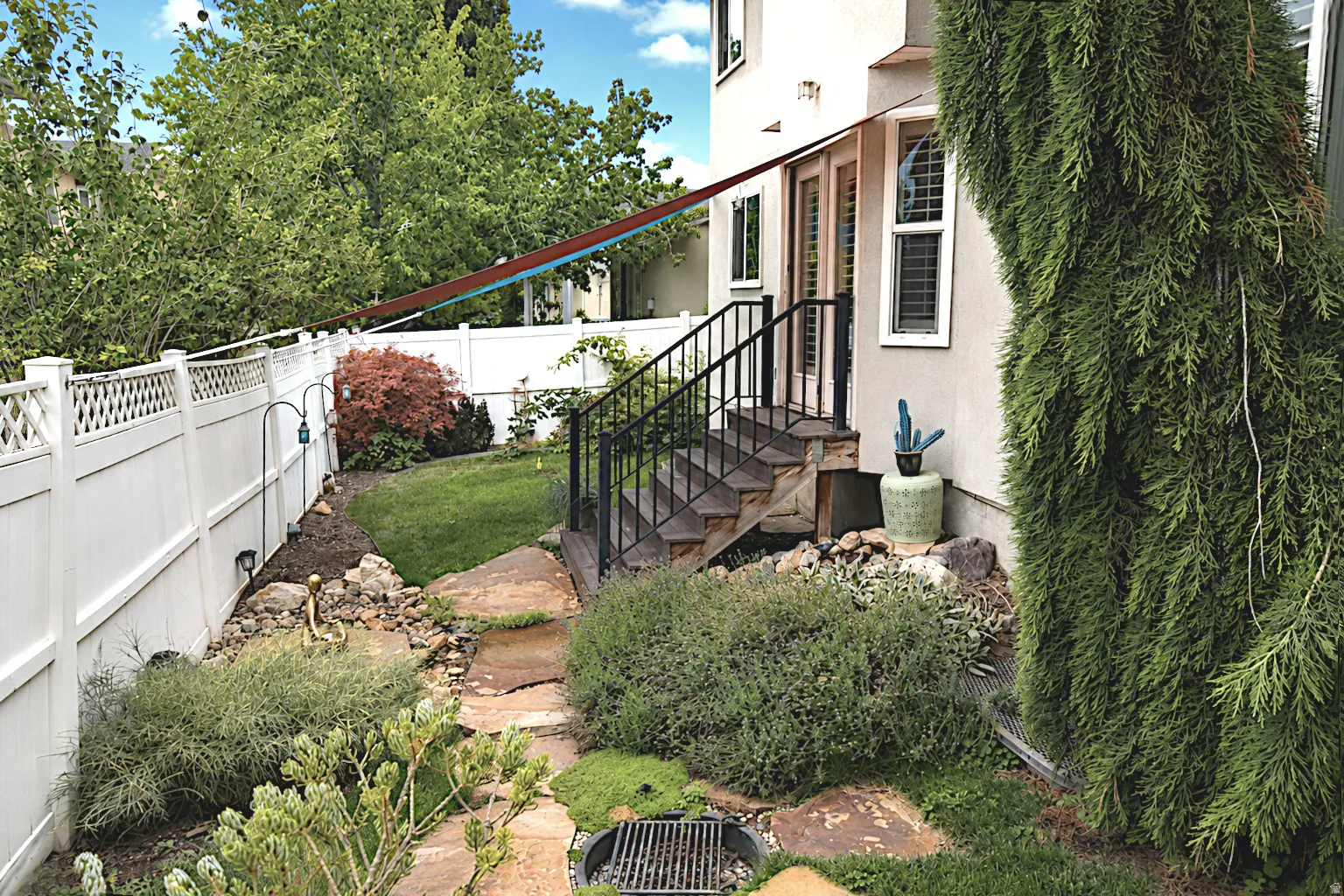 Backyard featuring a stone pathway, mature plantings, and a white lattice-top fence