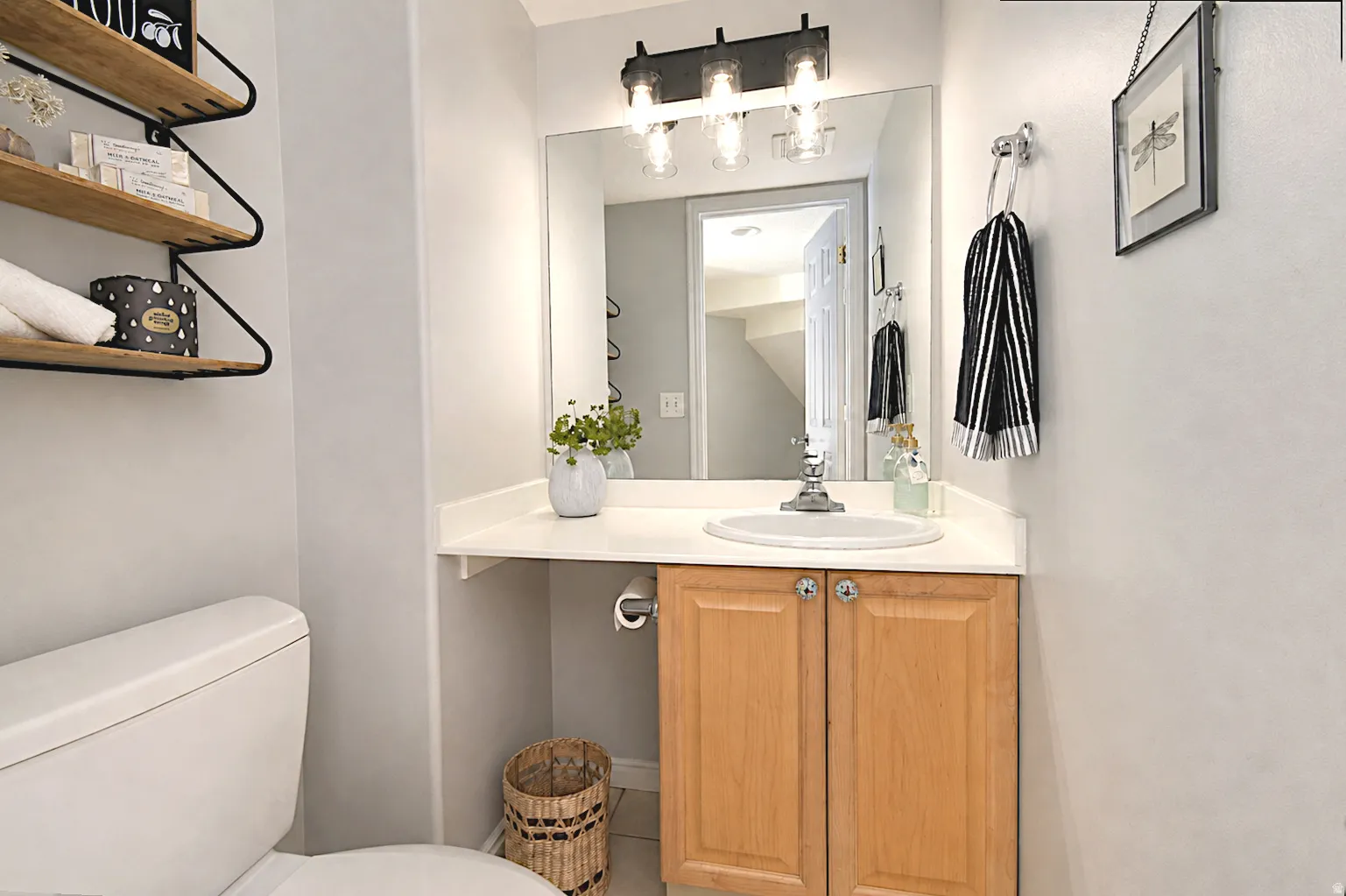 Vanity with a white countertop and integrated sink, natural wood-finish cabinetry, wall-mounted mirror, and a three-light fixture