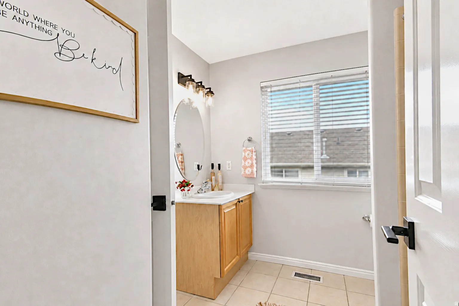 Wood-finish vanity with white sink, contemporary mirror, and a window with blinds