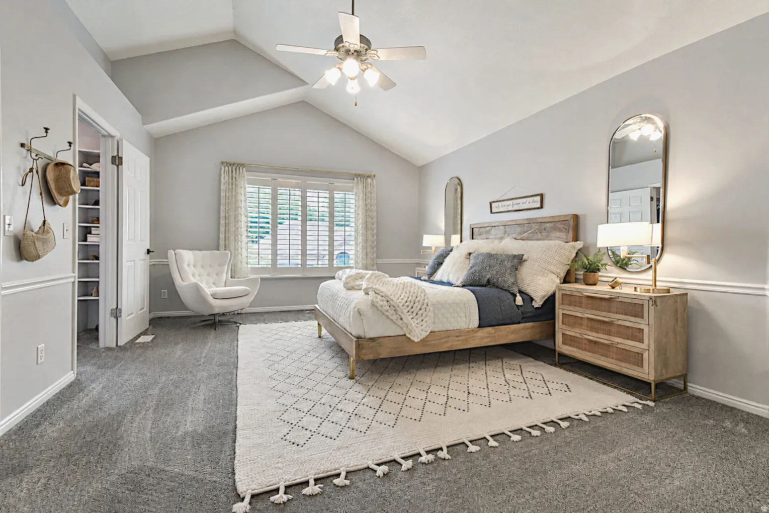 Vaulted ceiling with a ceiling fan, carpeted flooring, window with plantation shutters, and a built-in closet system