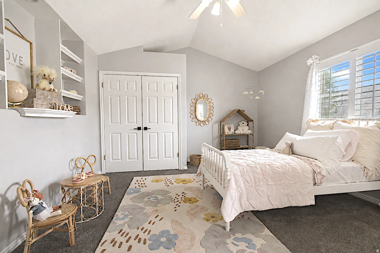 Vaulted ceiling with a ceiling fan, window with louvered shutters, carpeted flooring, and built-in wall shelving