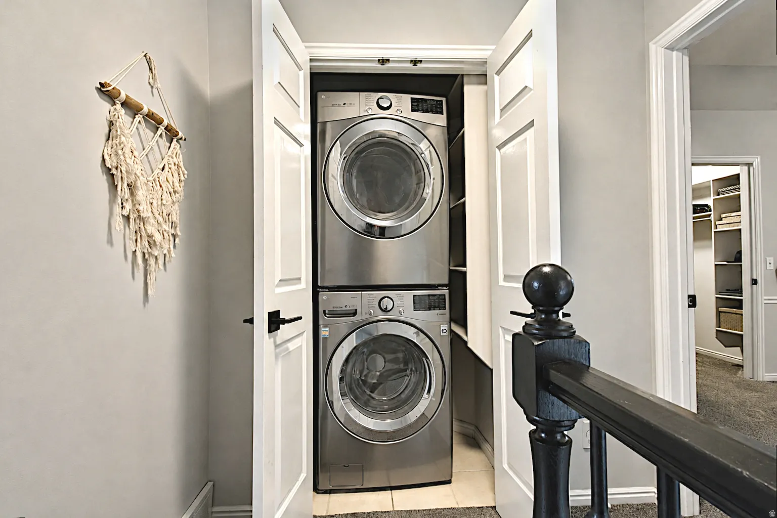 Conveniently located laundry closet featuring a stacked washer and dryer, adjacent to a hallway with carpeted flooring and a built-in shelving unit