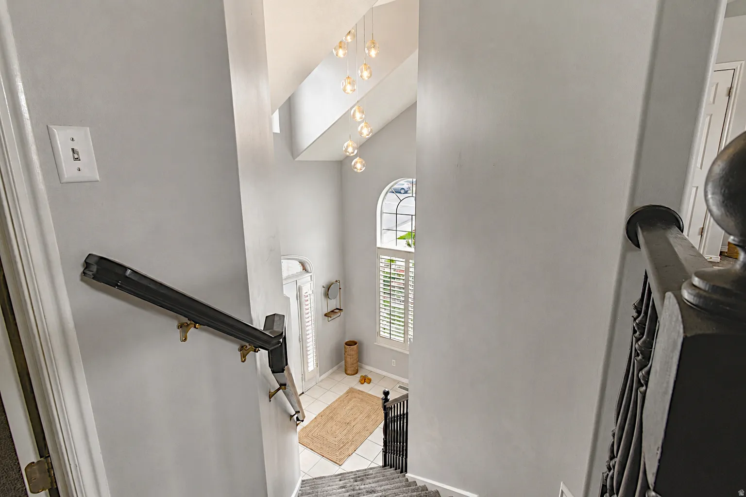 Two-story entry with arched window, plantation shutters, and a multi-pendant light fixture