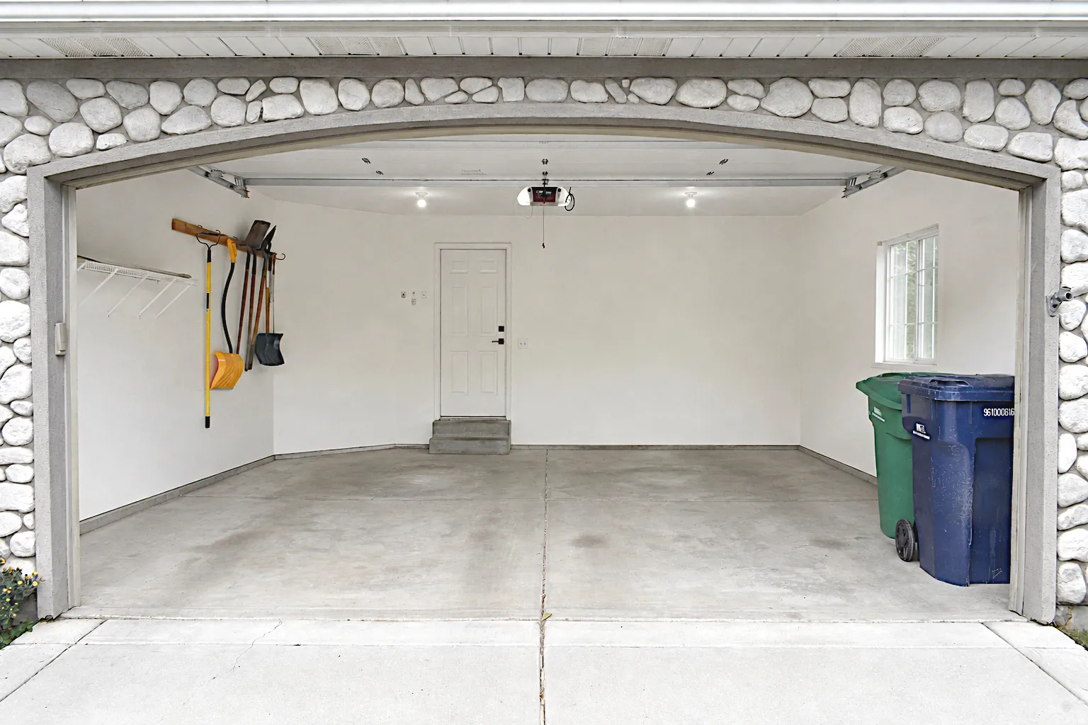 Spacious garage with concrete flooring, stone archway, interior access door, transom window, and overhead lighting