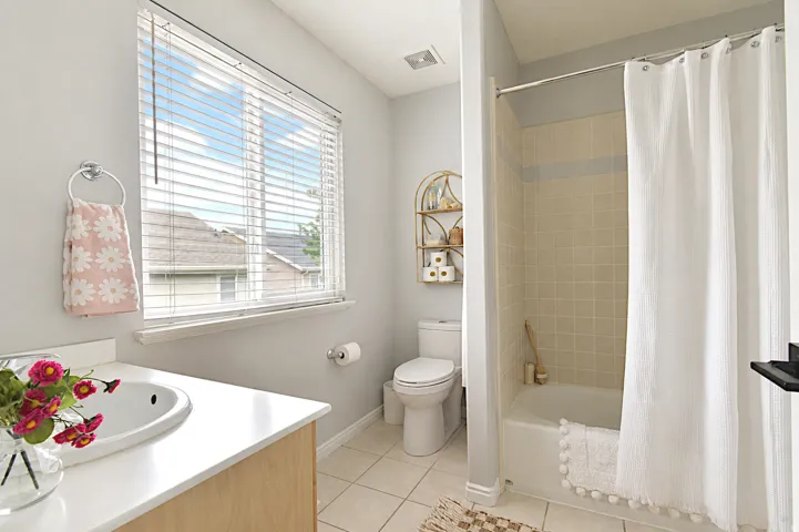 Window with horizontal blinds, built-in vanity with countertop and integrated sink, ceramic tile flooring, and a shower-over-tub combination with tiled walls