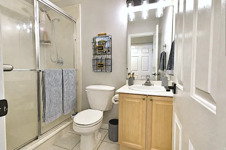 Shower enclosure with sliding glass door, single vanity with wood-finish cabinetry, built-in mirror, and overhead light fixture