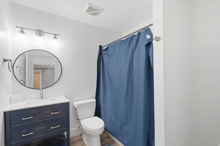 Vanity with a white countertop and blue cabinetry, oval mirror with a black frame, and wood-finish flooring