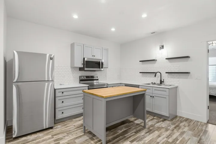 Modern kitchen featuring stainless steel appliances, white subway tile backsplash, light gray cabinetry, a wood-finish island, and wood-finish flooring