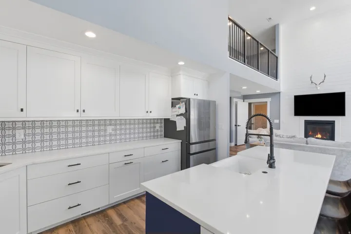 Open-concept kitchen with white shaker cabinetry, patterned tile backsplash, and wood-finish flooring